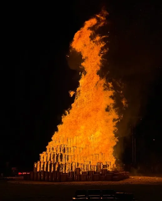 A tall pyre fully engulfed in flames against a black sky