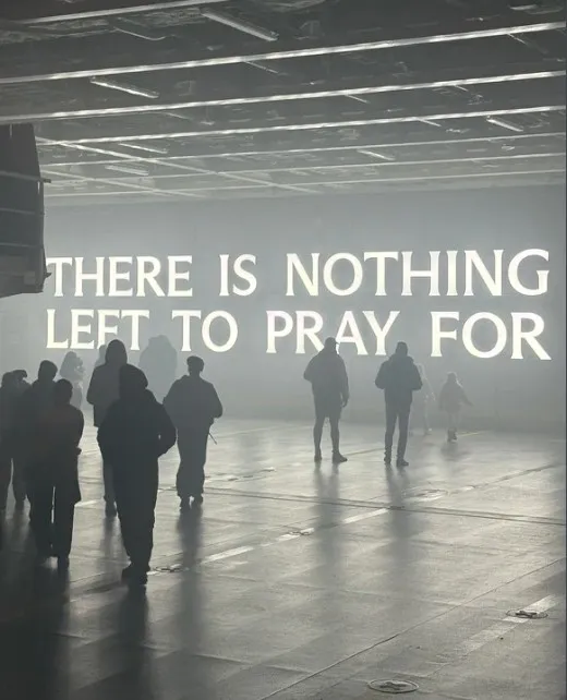 Figures in a hazy hall beneath the glowing words There Is Nothing Left To Pray For