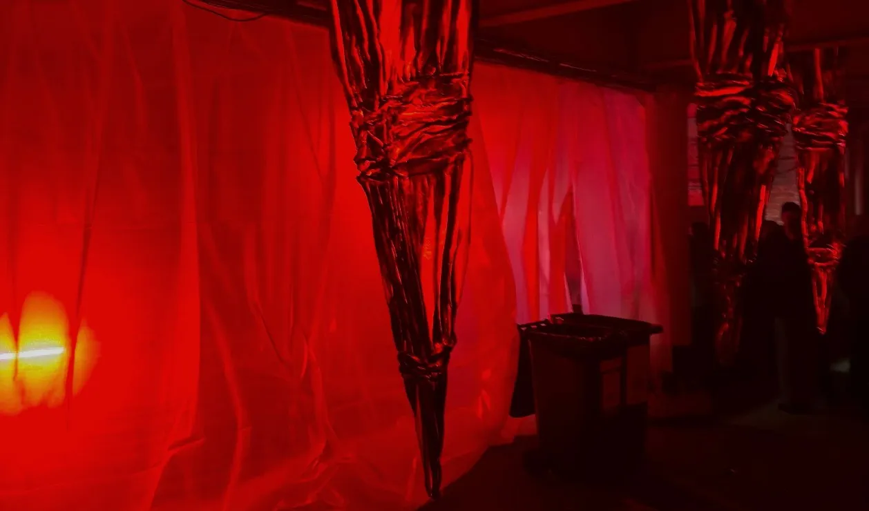 Crumpled silver sculptures hang like stalactites in a room washed with red light